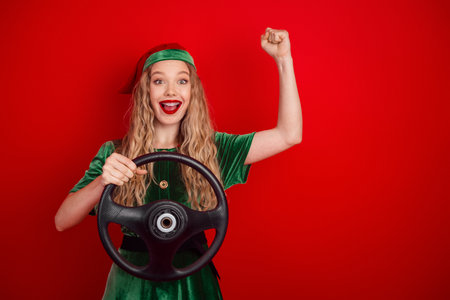 Excited young woman in a Christmas elf costume holding a steering wheel and celebrating a victory...