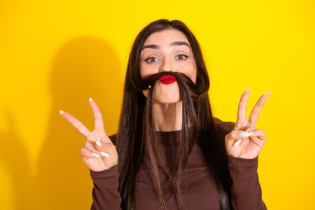 Charming brunette woman playfully posing with a vibrant expression against a bright yellow backgroundの写真素材