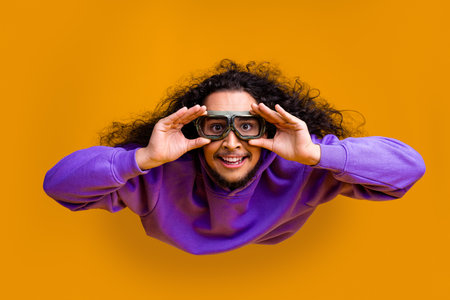 Funky man with curly hair wearing a purple hoodie making a fun facial expression on a vibrant orange...