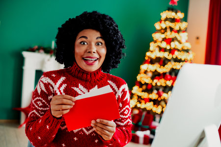 Excited woman opening Christmas card in festive room with decorated tree and holiday lights