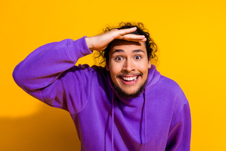 Happy young man wearing a purple hoodie over a vibrant yellow background posing with an expressive...