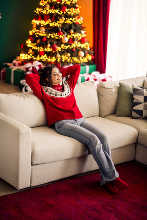 Young woman enjoying the cozy Christmas atmosphere at home with festive decorations and a beautifully lit Christmas tree.の写真素材