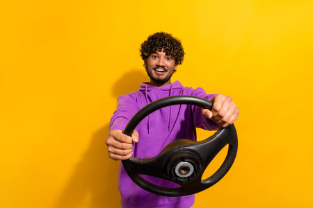 Cheerful man in vibrant hoodie holding a steering wheel against bright yellow background exuding fun and dynamic vibesの写真素材