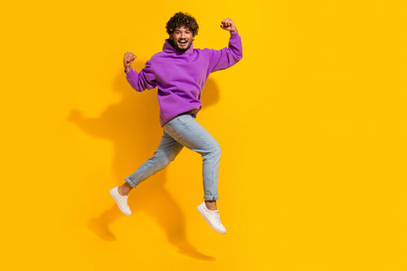 Happy young man jumping with energy in casual outfit against vibrant yellow background symbolizing...