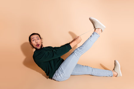 Young man sitting in a playful pose with casual fashion, wearing a green sweatshirt and jeans...