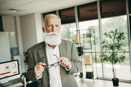 Professional mature male entrepreneur in elegant office attire standing confidently in a modern workspace settingの写真素材