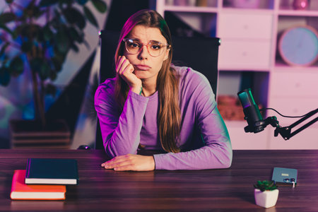 Young female blogger in casual purple attire preparing content at her home office with a microphone...