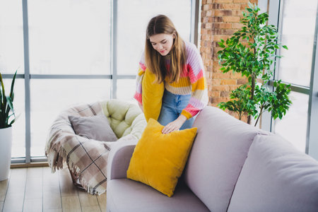 Woman decorating her cozy living room in a modern apartment with comfy furniture and vibrant details, creating a warm and inviting ambianceの写真素材