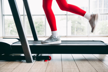 Side view of a woman in stylish red activewear using a treadmill inside a bright, modern gym setting...