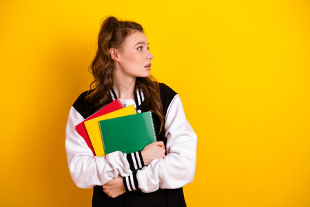 High school student holding colorful notebooks while looking to the side against a bright yellow backgroundの写真素材