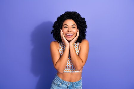 Cheerful young woman with curly hair smiling against purple background, radiating joy and happiness...