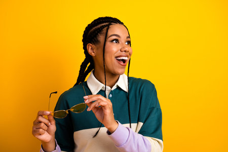 Young woman with braids and stylish eyewear, expressing happiness against vibrant yellow background,...