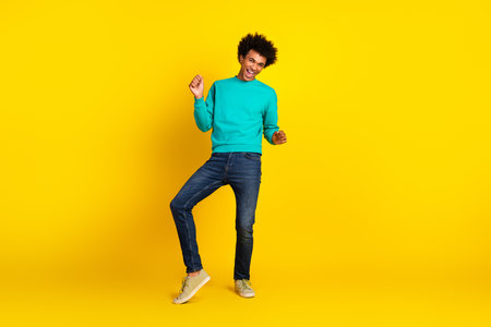 Young man in teal sweatshirt poses playfully against a vibrant yellow background, emphasizing...