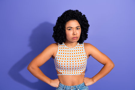 Confident young woman posing with determined expression, wearing casual top against violet...