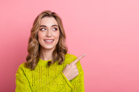 Cheerful young woman in a vibrant yellow sweater against a pink backdrop, radiating happiness and charmの写真素材