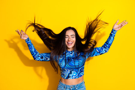 Young happy woman with flowing brunette hair enjoying a cheerful moment against vibrant yellow...