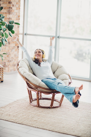 Young woman relaxing in a modern cozy living room chair enjoying leisure time with natural daylight in a stylish apartmentの写真素材