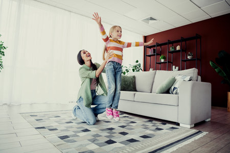 Mother and daughter enjoying playful moments together at home in the living room, creating bonding and joyful memoriesの写真素材