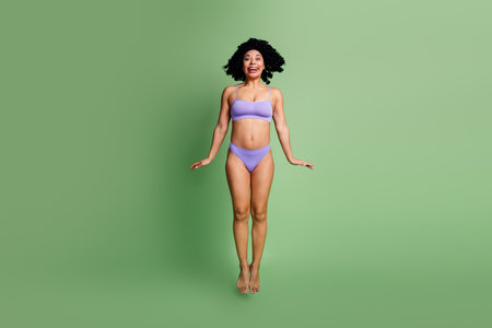 Confident young woman in lavender lingerie smiling against a green background showcasing natural beauty and positivityの写真素材