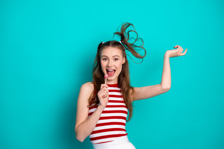 Cheerful young woman enjoying a fun moment with a bright smile, posing playfully with a vibrant turquoise backdropの写真素材