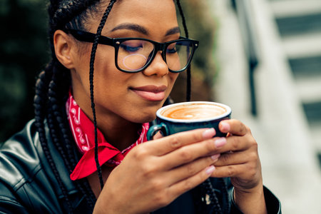 Stylish young woman enjoying a warm cup of coffee outdoors in a relaxed urban setting during a beautiful autumn dayの写真素材