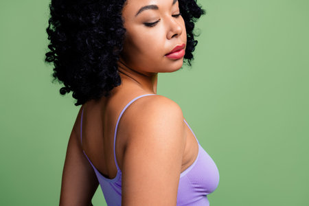 Stunning Woman with Curly Hair Posing in Soft Lighting with Confidence and Beauty on a Bright Green Backgroundの写真素材