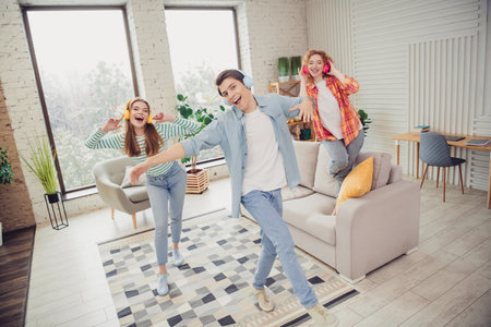 Three young friends dancing with headphones in a cozy living room showcasing a vibrant atmosphere of joy and togethernessの写真素材