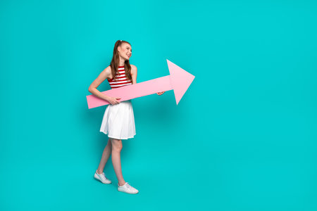 Young woman with a pink arrow in her hands, standing against a teal background and sharing a...