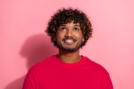 Portrait of a young man with a curly hairstyle and cheerful expression against a vibrant pink backdropの写真素材