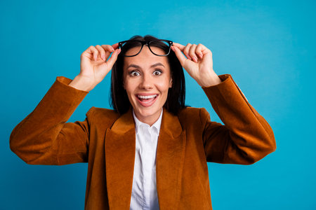 Confident businesswoman in retro-styled formal attire adjusting glasses against blue backgroundの写真素材