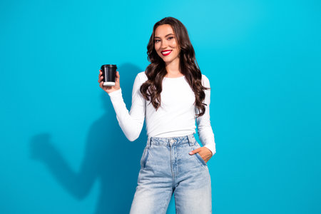 Young woman in casual attire with coffee cup posing against vibrant blue background, exuding...