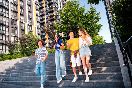 Four friends enjoying camaraderie outdoors on stairs at a city street against a modern urban backgroundの写真素材