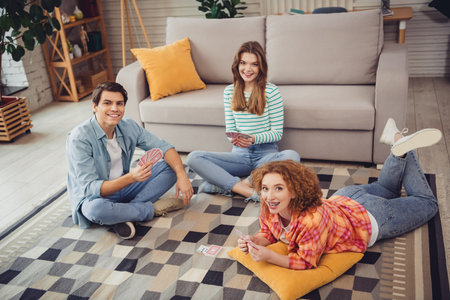 Young friends enjoying a card game with laughter and relaxation in a cozy modern home during the afternoon sunlight.の写真素材