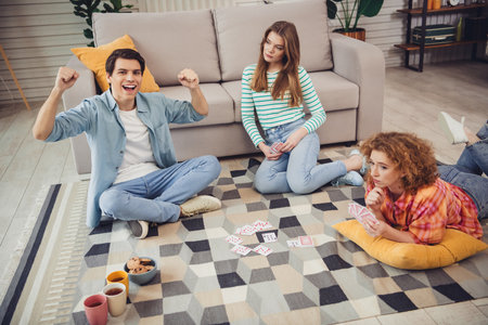Young friends playing cards in a cozy living room with snacks and drinks, showcasing relaxation and friendly competitionの写真素材