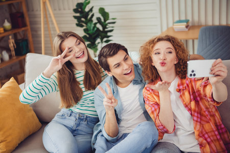 Group of young friends taking a selfie together on a sofa in a bright home interior during daytime