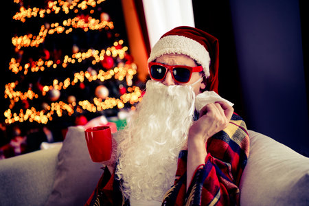 Funny Santa enjoying a cozy Christmas at home by the tree with decorations and garlands.の写真素材