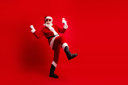 Santa Claus in a vibrant pose holding a smartphone against a bold red background, celebrating festive cheerの写真素材