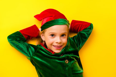 Joyful child wearing red and green Christmas elf costume with a vibrant yellow background expressing a cheerful seasonal moodの写真素材