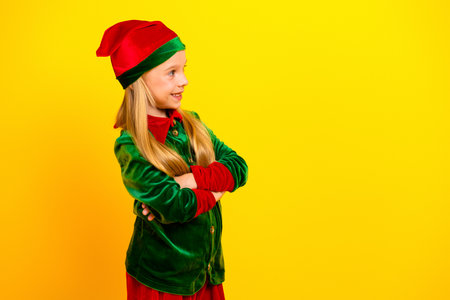 Young girl dressed as a Christmas elf in a colorful costume standing confidently against a vibrant yellow backgroundの写真素材