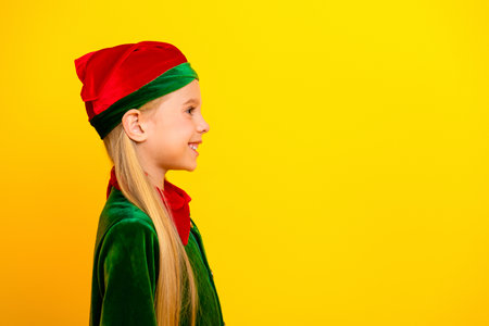 Smiling girl wearing festive elf costume on vibrant yellow background, radiating holiday cheer and...