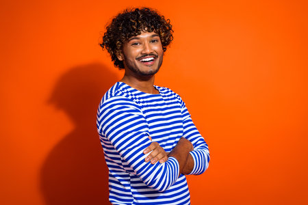 Young man in a striped sailor-style shirt smiling confidently against a bright orange background, showcasing cheerful vibesの写真素材