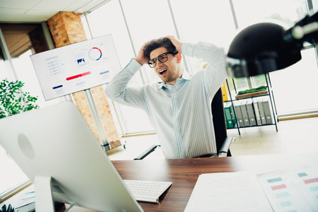 Young professional businessman frustrated in front of a computer with charts displayed in a modern...