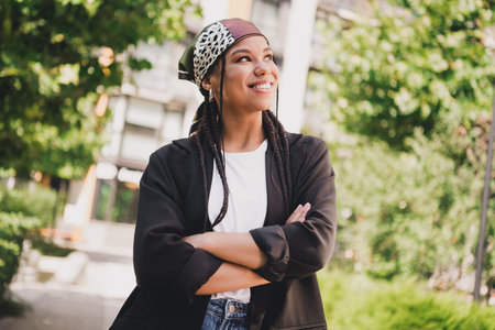 Playful urban fashionista smiling outdoors in stylish casual outfit with headscarf and braided hair