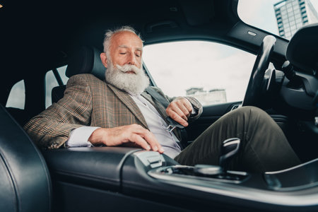 Confident mature gentleman in a stylish suit seated inside modern car in urban setting during daylightの写真素材