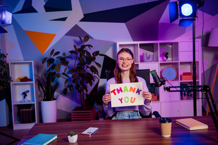 Young female blogger holding thank you sign in colorful studio with creative decor and professional podcasting setupの写真素材