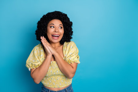 Portrait of a joyful young woman posing with her hands clasped against a vibrant blue background