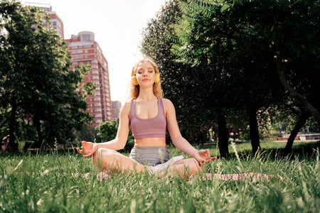 Young woman practicing yoga outdoors in an urban park setting, enjoying relaxation and physical wellness during sunny weather.の写真素材