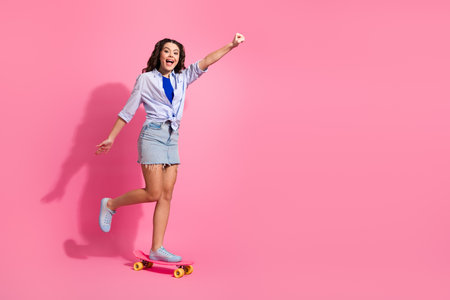 Young cheerful girl on a skateboard showcases vibrant youthful enthusiasm on a bright pink background, symbolizing joy and lifestyleの写真素材
