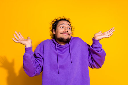 Confused man in a purple hoodie expressing a casual shrug gesture with a cheerful mood on a bright...