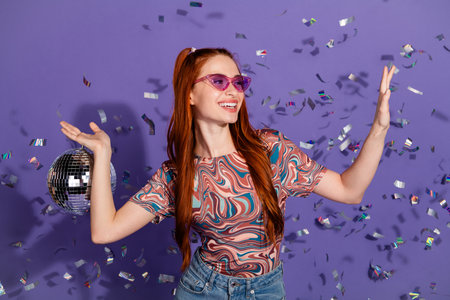 Young vibrant woman enjoying a festive atmosphere with confetti on purple background embracing...